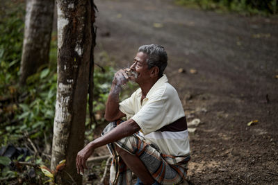 Side view of senior man sitting and smoking cigarette on the side of the road