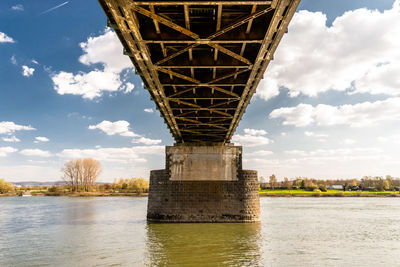 Steel, lattice structure of a railway bridge over a river with a background of blue sky with clouds