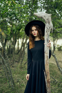 Portrait of young woman standing against trees