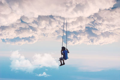 Digital composite image of boy swinging over sky
