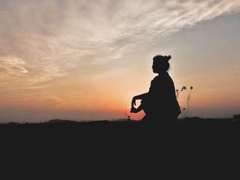 Silhouette woman crouching against orange sky