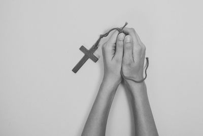 Cropped hands holding rosary against gray background