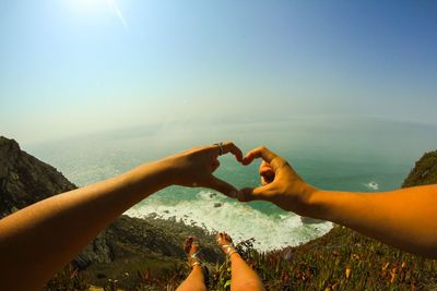 Close-up of couple making heart shape on mountain by sea