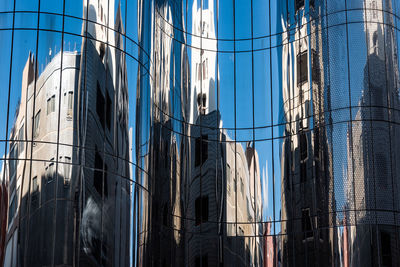 Low angle view of reflected modern buildings against clear blue sky