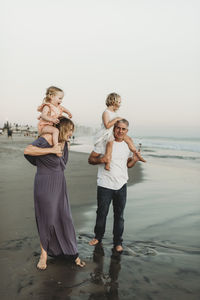 Lifestyle image of mother and father holding young daughters on should