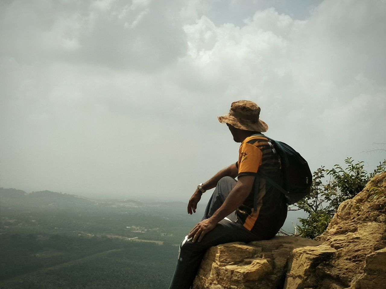 MAN SITTING ON ROCK LOOKING AT MOUNTAIN