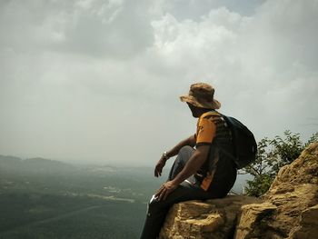 Man sitting on rock looking at mountain against sky