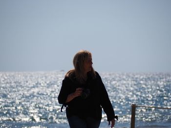 Young woman standing on sea against clear sky