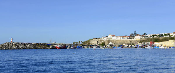 Sailboats in sea by buildings against clear blue sky