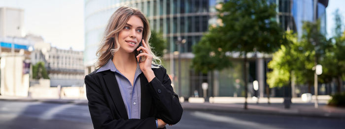Young businesswoman talking on mobile phone while standing in city