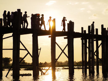 Silhouette people standing on bridge against sky during sunset