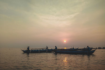 Silhouette people on boat in sea against sky during sunset