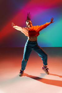 Energetic happy female dancer in tiptoe with outstretched arms in light colorful in studio with eyes closed