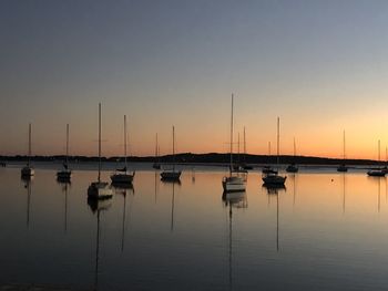 Sailboats moored in lake at sunset