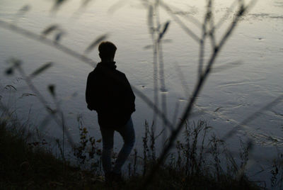 Silhouette man standing by lake at sunset