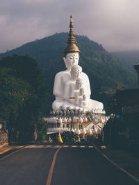 Statue by temple against building and mountain against sky