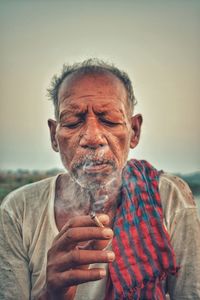 Close-up of mature man smoking beedi against clear sky