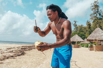 Side view of young man drinking water while standing at beach