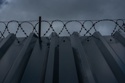 Low angle view of barbed wire fence against sky