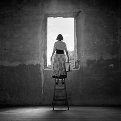 Rear view of woman standing on a ladder looking out window