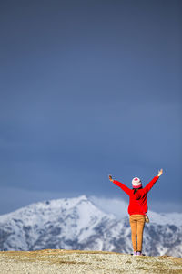 Full length of woman standing with arms raised on mountain against sky