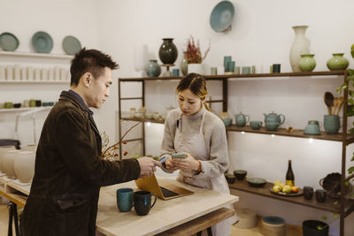 Side view of male customer paying through smart phone at pottery shop