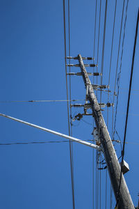 Low angle view of electricity pylon against clear blue sky