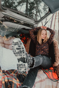 Blonde woman wrapped in blanket in trunk car. travel in winter. car decorated with festive 