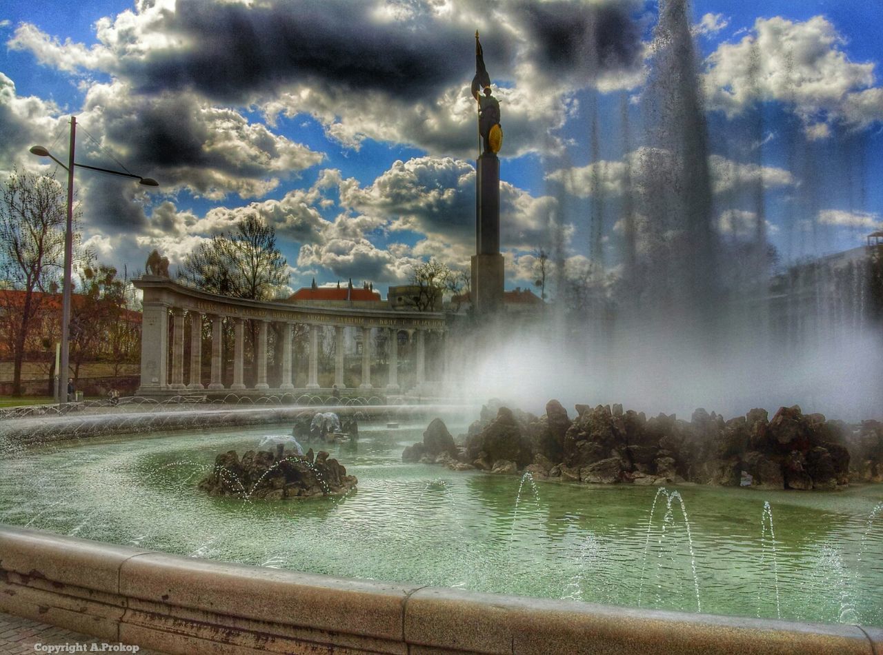 water, built structure, architecture, sky, fountain, cloud - sky, tree, building exterior, cloudy, river, splashing, cloud, reflection, motion, travel destinations, waterfront, nature, outdoors, flowing water, day