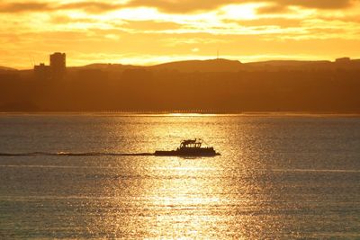 Silhouette motorboat on sea against sky during sunrise