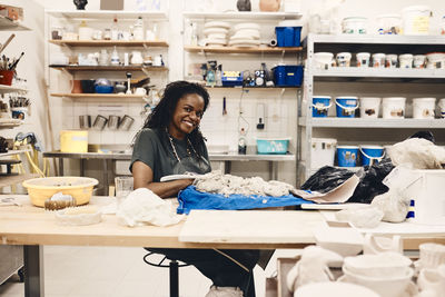 Full length portrait of smiling woman sitting at table in art class