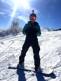 Full length of man with snowboard standing on snowy hill against sky during sunny day