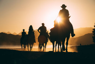 Silhouette people riding horses on beach during sunset