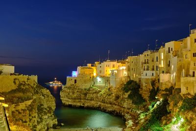 Illuminated buildings by sea against sky at night