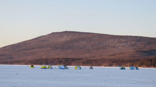 Tents on snow covered landscape against mountain during sunset