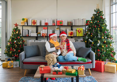 Happy senior caucasian couple sitting on sofa couch cheers champagne flute together on christmas