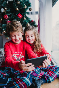 Brother and sister at home taking a selfie with mobile phone.kids sitting by christmas tree