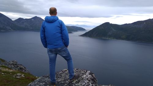 Rear view of man standing on rock looking at mountains