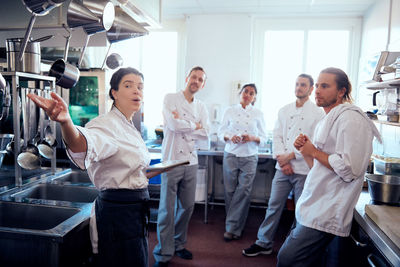 Mid adult female chef with digital tablet discussing with colleagues in commercial kitchen