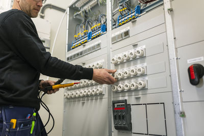 Midsection of repairman with voltage tester repairing switchboard in industry