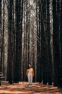 Full length of woman standing amidst trees in forest