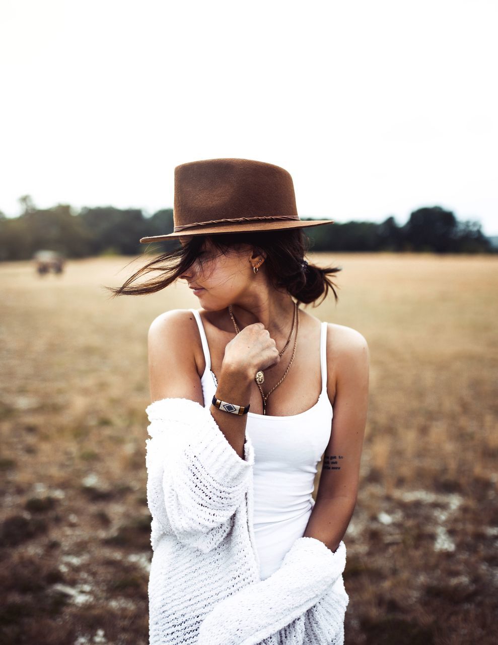 one person, standing, hat, focus on foreground, clothing, young adult, waist up, lifestyles, leisure activity, real people, land, day, young women, casual clothing, field, nature, front view, sky, fashion, outdoors, hairstyle, beautiful woman