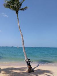 Woman leaning on palm tree at beach