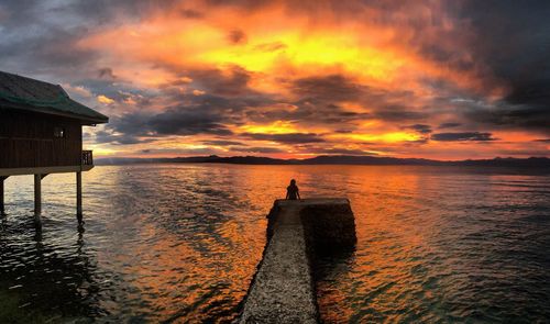 Rear view of woman sitting on pier over sea during sunset