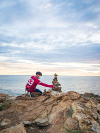 Men sitting on rock by sea against sky