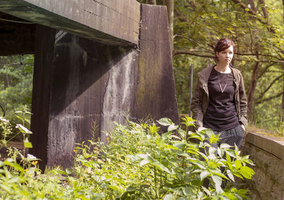 Beautiful woman standing by retaining wall in forest