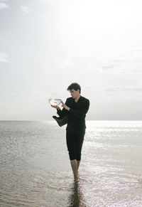 Full length of man drinking water in sea against sky