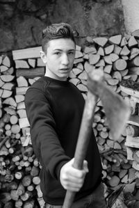 Portrait of teenage boy holding axe against stacked firewood