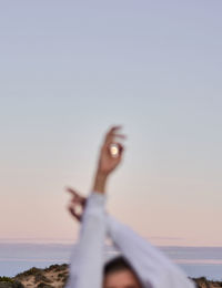 Unrecognizable crop female standing with raised arms on background of sunset sky with moon and enjoying freedom during vacation in summer