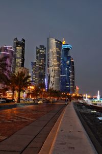 Illuminated street amidst buildings against sky at dusk